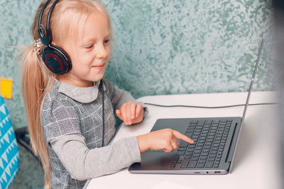 Cute girl wearing headphones while using laptop on table