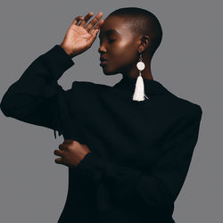 Young woman wearing black casual clothing and white earrings against gray background