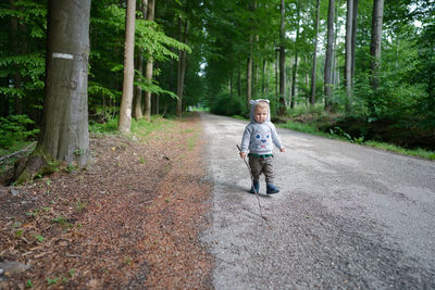 Baby boy with branch wood walking on the road alone in the forest