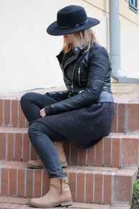 Woman wearing hat sitting against wall