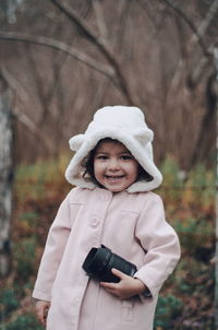 Cute girl in warm clothing holding camera lens while standing on field