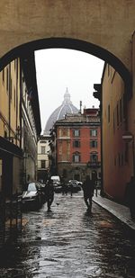 People walking on wet street amidst buildings in city