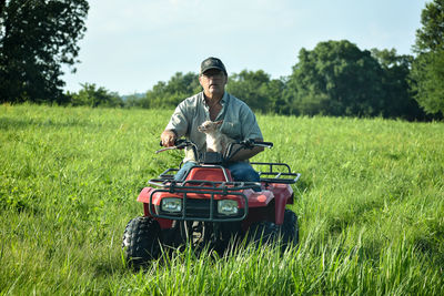 Man holding dog while riding quadbike in field