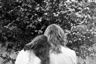 Rear view of female friends standing against flowering plant