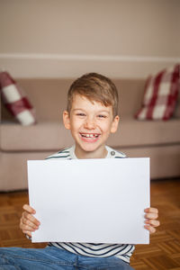 Portrait of smiling boy holding blank paper while sitting at home