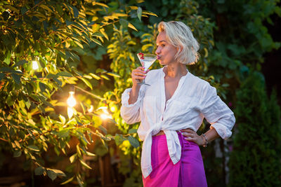 Young woman standing against trees during sunset