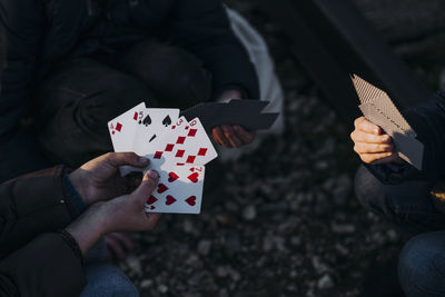 Crop hands of three children playing cards while sitting in a train track