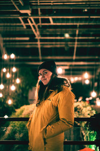 Portrait of woman standing against illuminated light at night