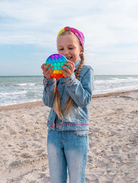 Happy child rainbow pop it toy beach girl walking on sea background antistress sensory simple dimple