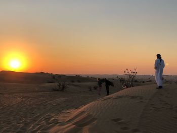 Rear view of man standing on sand dune during sunset