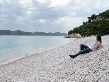 Side view of woman relaxing on beach against sky