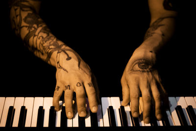 Tattooed mans hands on the keyboard of a piano. dark background