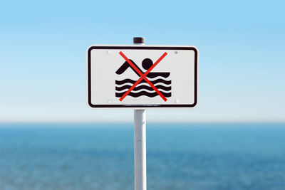 Close-up of road sign by sea against clear sky