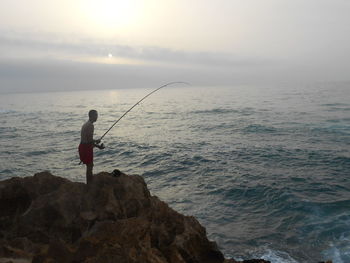 Man fishing in sea against sky