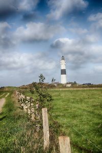 Lighthouse on field by building against sky