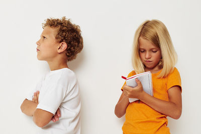 Sister writing in notebook standing by angry brother