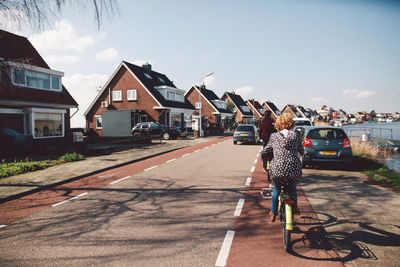 Rear view of woman riding bicycle on street against sky