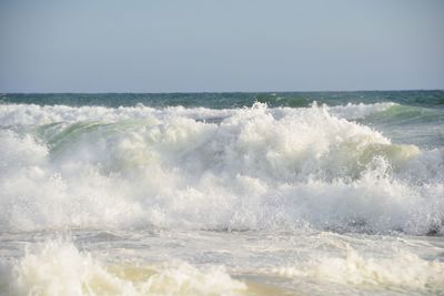 Waves splashing in sea against clear sky