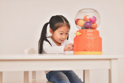 Cute girl playing with ball dispenser at table against wall