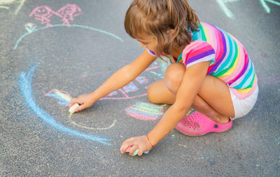 Playful girl drawing with chalk on footpath