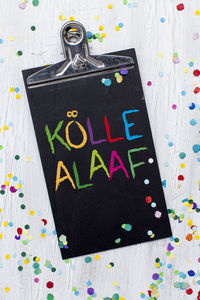 Directly above shot of text on clipboard with colorful confetti at table