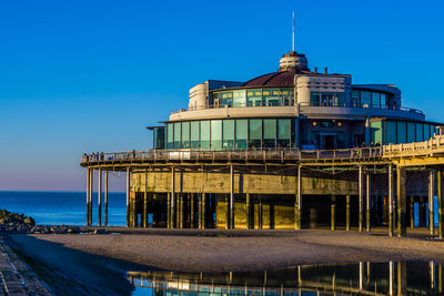 Building by sea against clear blue sky