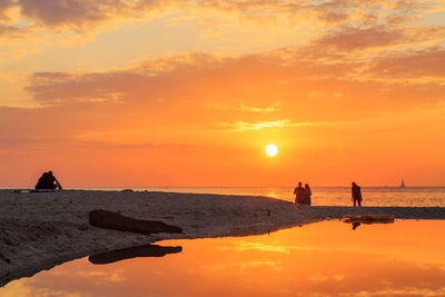 Silhouette people on beach against sky during sunset