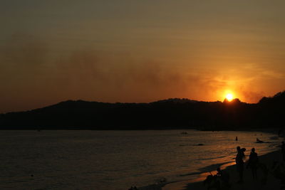 Silhouette people on beach against sky during sunset