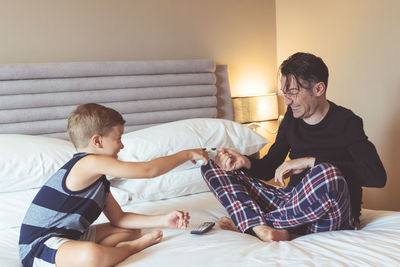 Father and son playing while sitting on bed at home