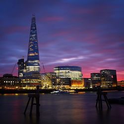 Shard london bridge by thames river against cloudy sky in city at dusk