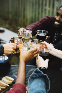 Cropped image of friends toasting drinks while sitting in backyard