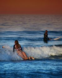 People surfing on sea against sky during sunset