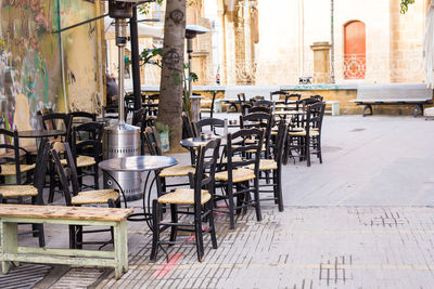 Empty chairs and tables at sidewalk cafe amidst buildings