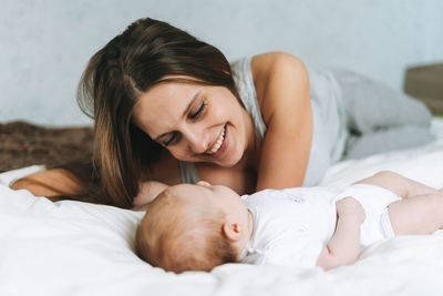 Young mother having fun with cute baby girl on the bed with white linen, natural tones, love emotion