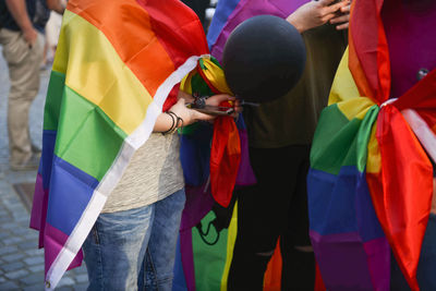 Low section of friends standing on multi colored umbrella