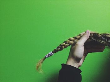 Cropped hand holding braided hair against green background