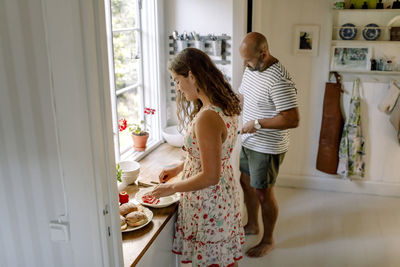 Side view of daughter and father arranging food while standing in kitchen