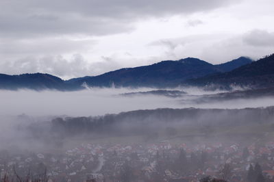 Townscape by mountains against sky during foggy weather