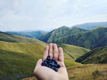 Cropped image of hand on mountain against sky