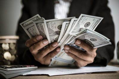 Midsection of businessman holding paper currency on table