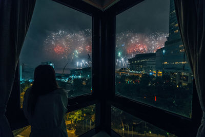 Rear view of woman looking through window in city