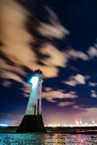 Lighthouse by sea against sky at night