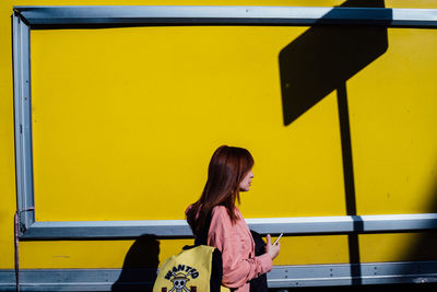 Side view of young woman against yellow wall