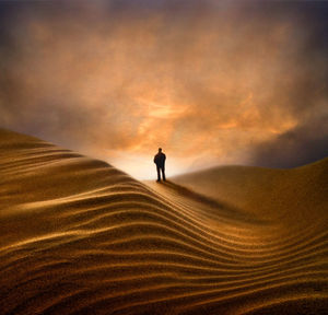 Silhouette man standing on sand dune against sky during sunset