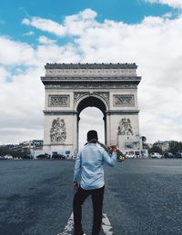 Rear view of man with saxophone standing against arc de triomphe