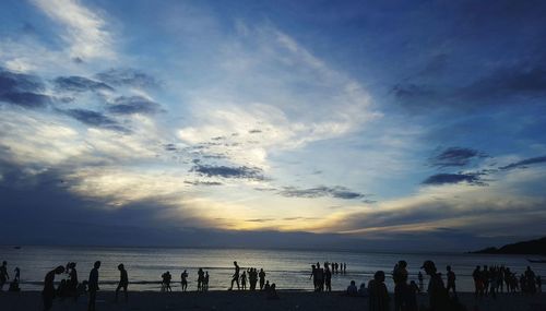 Silhouette people on beach against sky during sunset