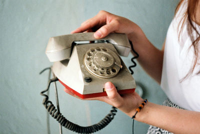 Midsection of woman holding rotary phone against wall at home