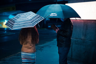 Rear view of woman with umbrella standing in rain