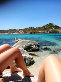 Low section of woman relaxing on beach against clear blue sky