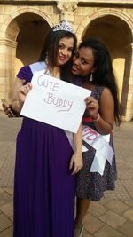 Portrait of smiling females showing placard while standing against building